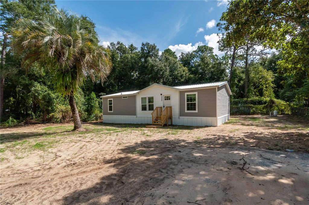 A single-story manufactured home with gray siding sits on a sandy lot near trees — 1143 SE 159TH COURT, SILVER SPRINGS, FL