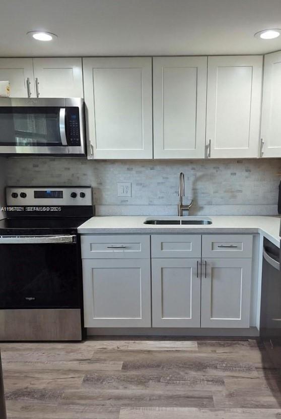 A kitchen features white shaker cabinets, stainless steel appliances, a tiled backsplash, and wood flooring — 7600 NW 5th Pl # 108, Margate FL 33063, MARGATE, FL