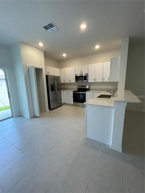 A kitchen features white cabinets, stainless steel appliances, and light-colored tile flooring — 10199 TRUMPET HONEYSUCKLE WAY, SAN ANTONIO, FL