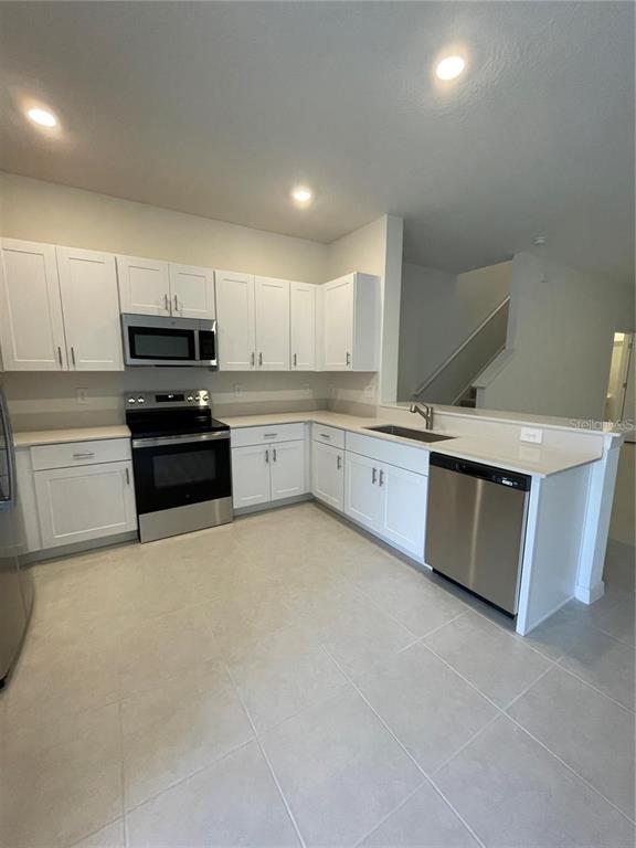 A kitchen features white cabinets, stainless steel appliances, and light-colored tile flooring — 10199 TRUMPET HONEYSUCKLE WAY, SAN ANTONIO, FL