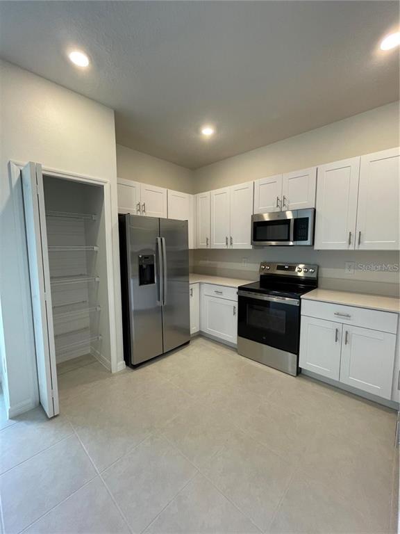 A kitchen features white cabinets, stainless steel appliances, and a walk-in pantry — 10199 TRUMPET HONEYSUCKLE WAY, SAN ANTONIO, FL