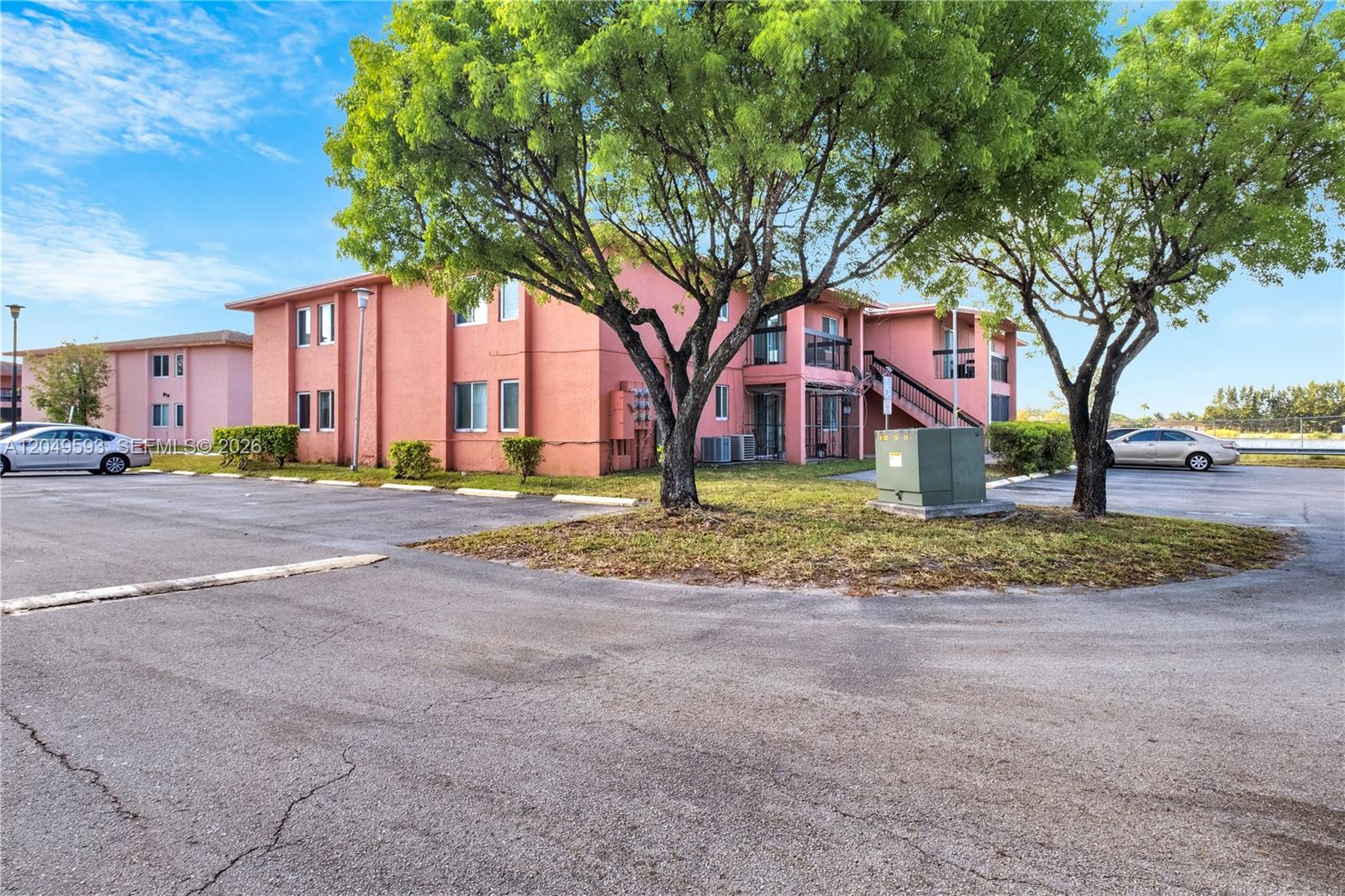 A two-story pink apartment building stands behind a parking lot with two large trees — 2020 NW 119th St # 1122, Miami FL 33167, MIAMI, FL