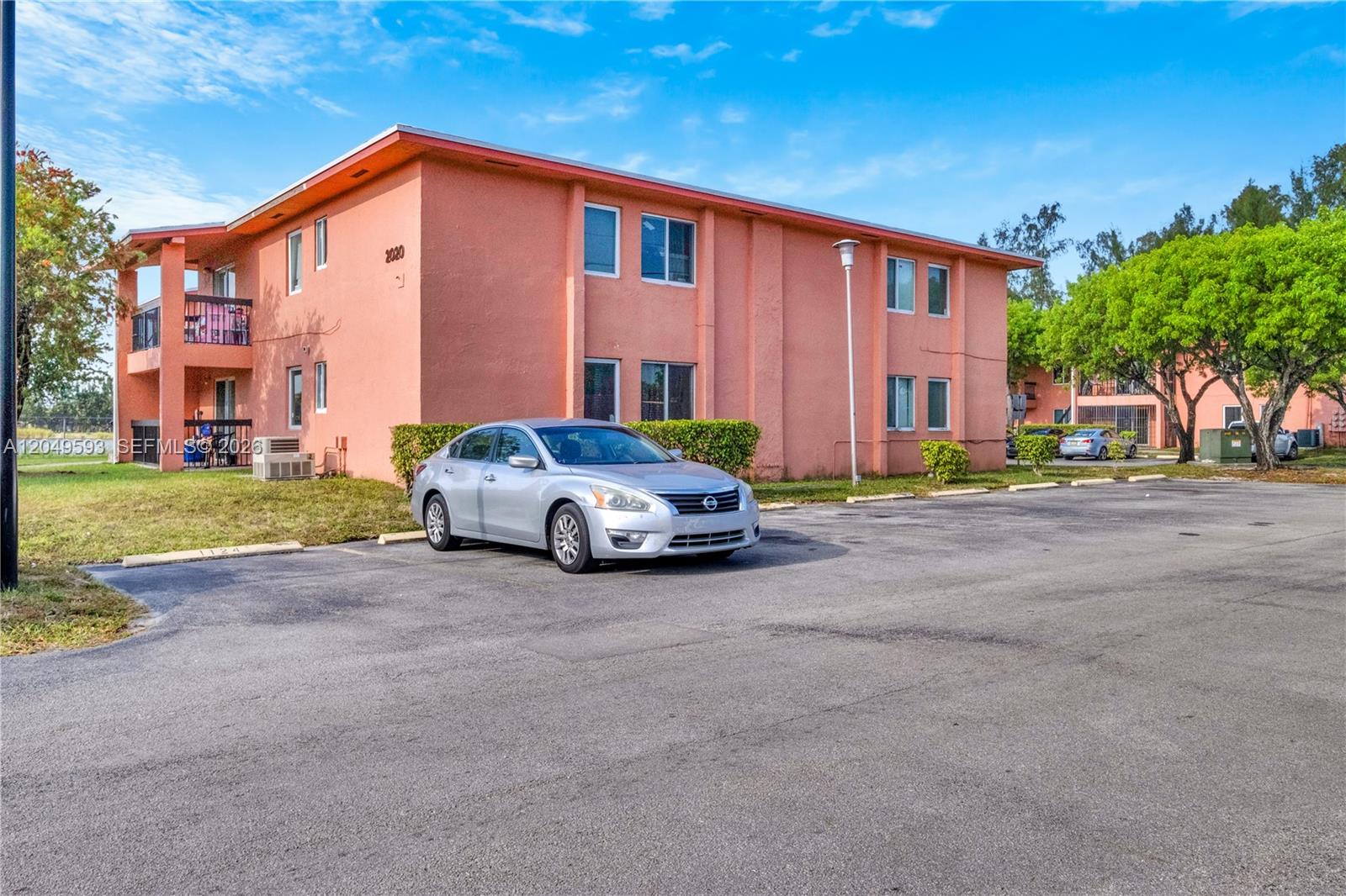 A silver sedan is parked in front of a two-story peach-colored apartment building — 2020 NW 119th St # 1122, Miami FL 33167, MIAMI, FL