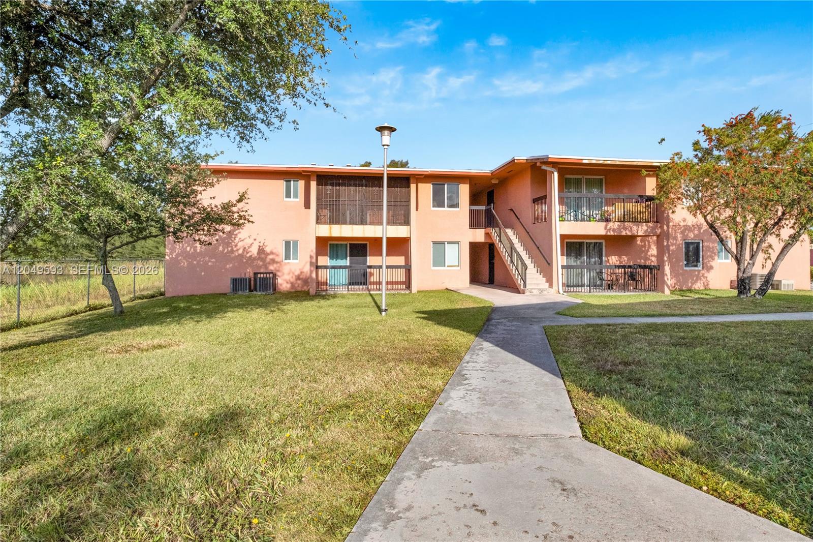 A two-story peach-colored apartment building features exterior staircases, balconies, and a concrete walkway — 2020 NW 119th St # 1122, Miami FL 33167, MIAMI, FL