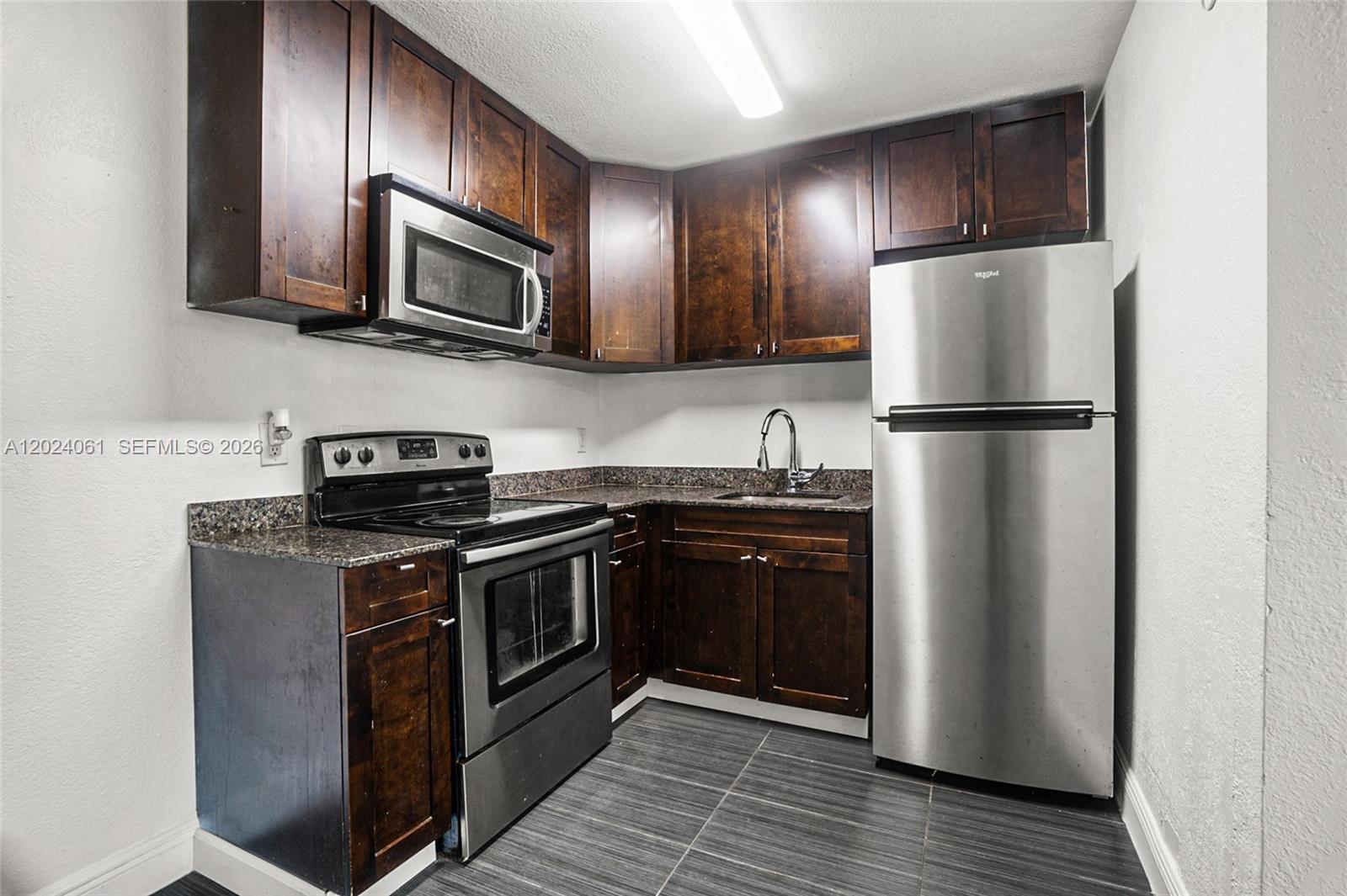A kitchen features dark wood cabinets, stainless steel appliances, and granite countertops — 37 SW 14th St # 16, Dania Beach FL 33004, DANIA BEACH, FL