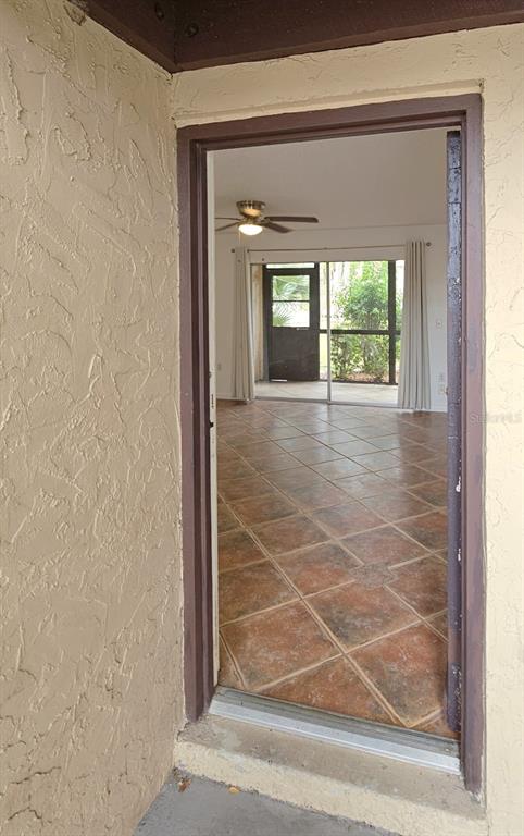 A doorway leads from a textured exterior wall into a room with brown tile flooring — 2724 HIDDEN LAKE BOULEVARD UNIT A, SARASOTA, FL