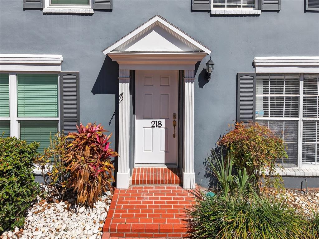 A white front door with the number 218 is framed by a portico and brick walkway — 218 S TAMPANIA AVENUE, TAMPA, FL