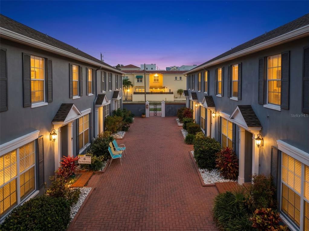 A brick courtyard sits between two rows of gray townhouses with lit windows at dusk — 218 S TAMPANIA AVENUE, TAMPA, FL