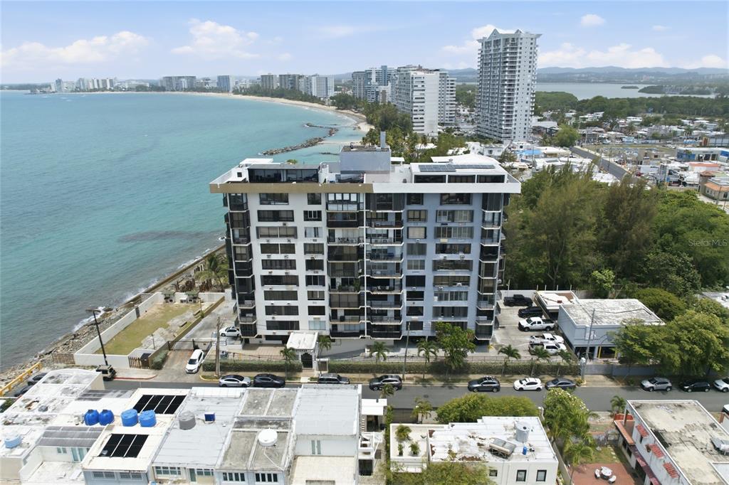 An aerial view shows a multi-story apartment building situated along a sandy beach coastline — INGA 1 N COSTAMAR CONDOMINIUM UNIT PH, SAN JUAN, PR