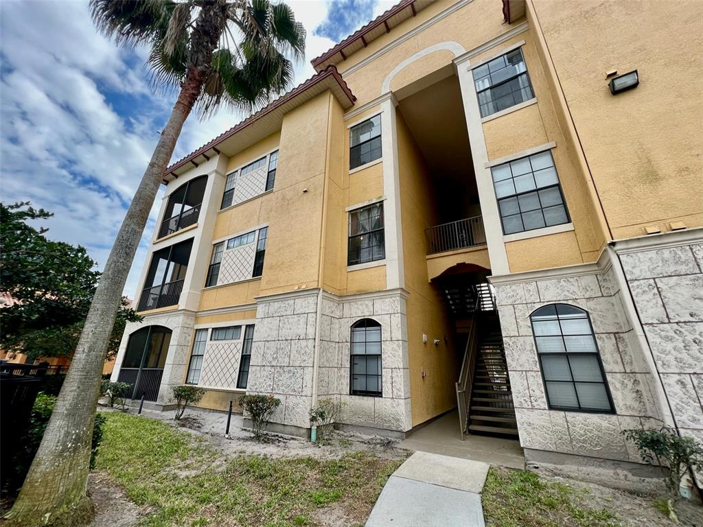 A three-story apartment building features yellow stucco walls, stone veneer accents, and exterior staircases — 6153 METROWEST BOULEVARD UNIT 308, ORLANDO, FL