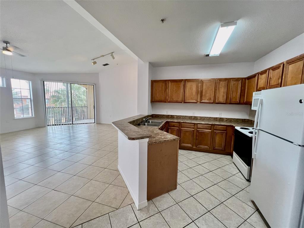 A kitchen with wood cabinets and a breakfast bar opens into a tiled living area — 6153 METROWEST BOULEVARD UNIT 308, ORLANDO, FL