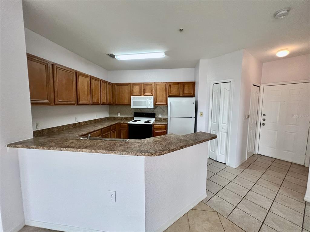 A kitchen features wood cabinets, laminate countertops, white appliances, and tile flooring — 6153 METROWEST BOULEVARD UNIT 308, ORLANDO, FL