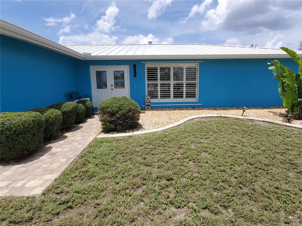 A bright blue house exterior features a metal roof, white shutters, and a stone walkway — 190 CASA LANE, PUNTA GORDA, FL
