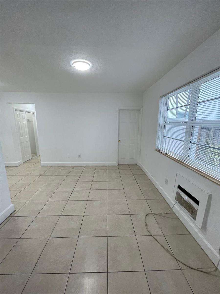 A room with white walls, beige tile flooring, a window with blinds, and an air conditioner — MIAMI BEACH, FL