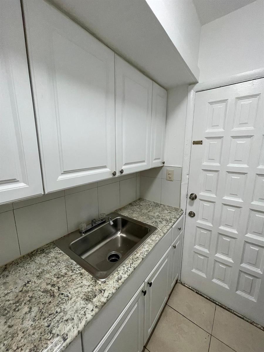 A kitchen sink with granite countertops and white cabinets next to a white paneled door — MIAMI BEACH, FL