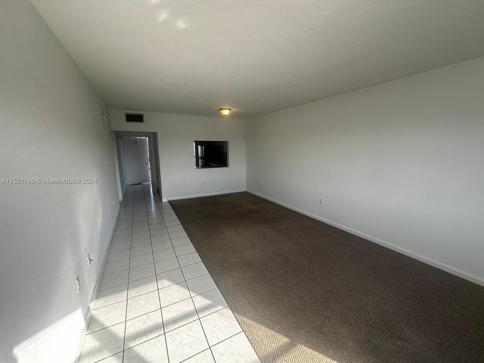 An empty room features a tiled entryway, brown carpeting, and a kitchen pass-through window — 18700 NE 3rd Ct # 626, Miami FL 33179, MIAMI, FL