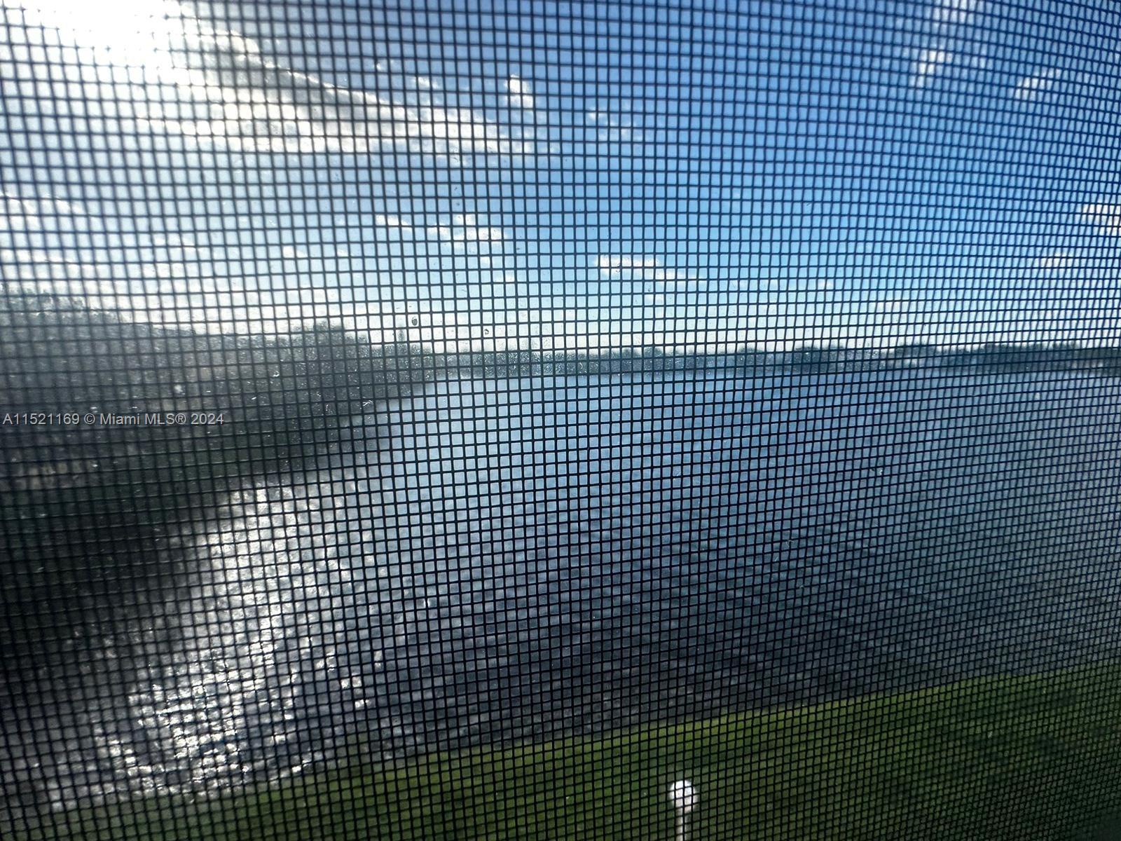 A view of a lake and grassy bank seen through a window screen — 18700 NE 3rd Ct # 626, Miami FL 33179, MIAMI, FL
