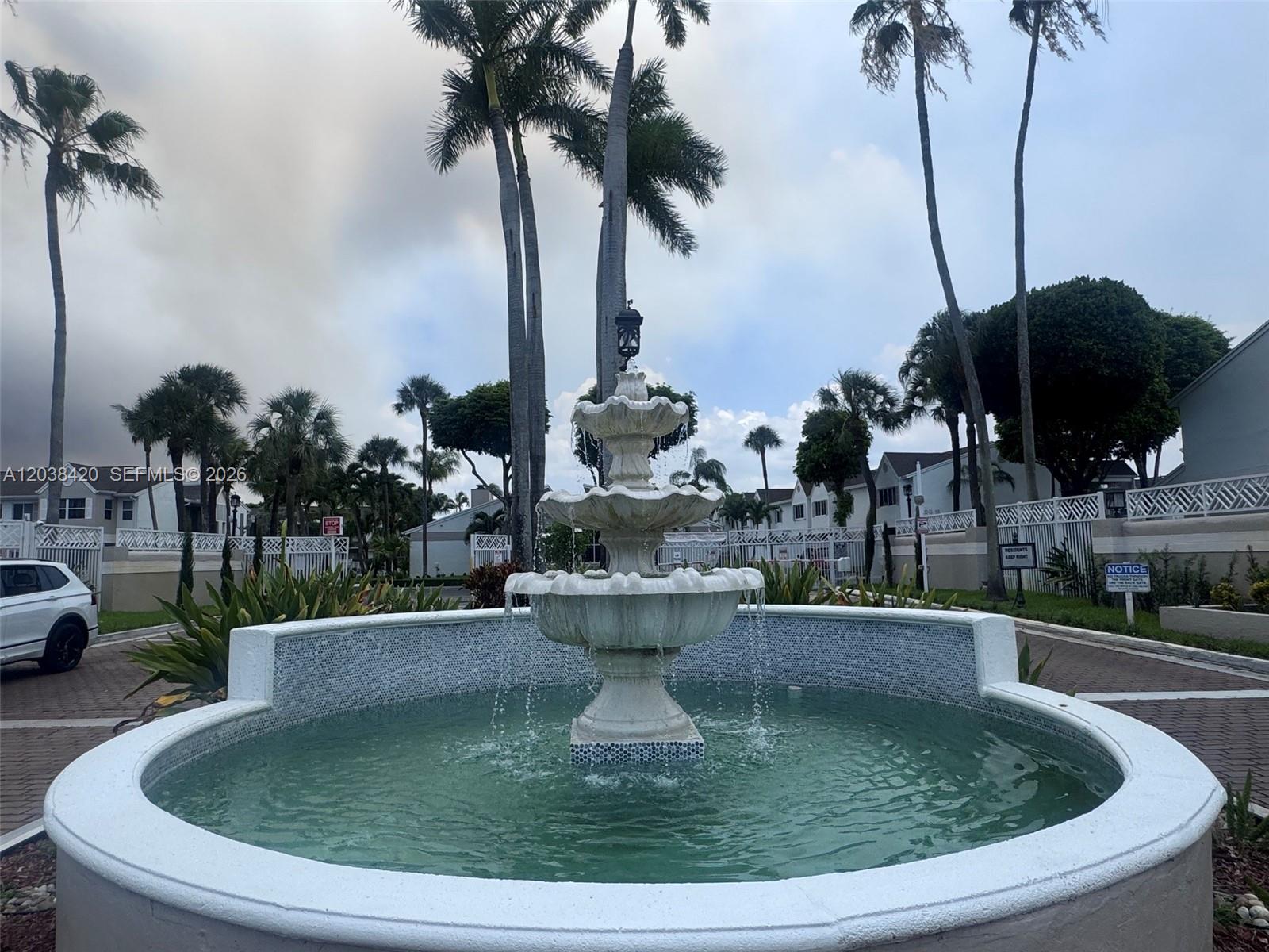 A three-tiered white fountain sits in the center of a circular pool outdoors — 17425 NW 67th Pl # 13, Hialeah FL 33015, HIALEAH, FL