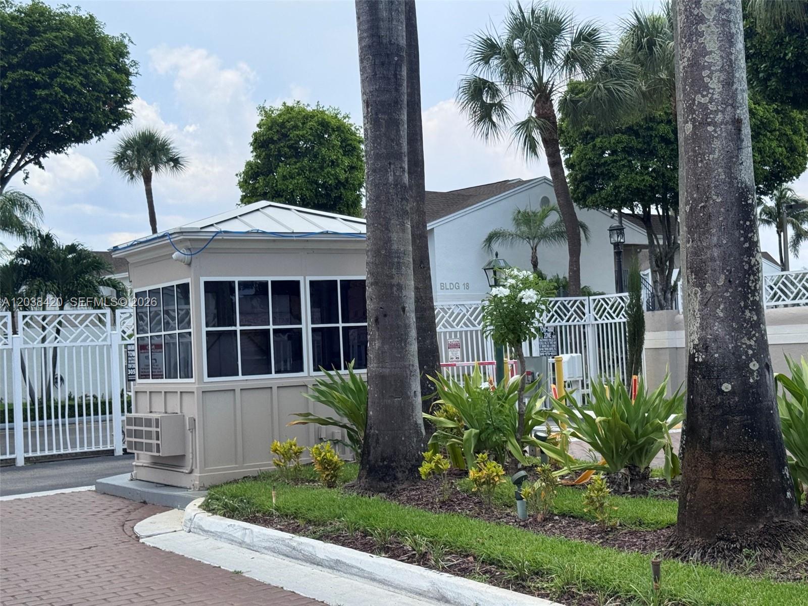 A small security guard booth stands in front of a white building and gated entrance — 17425 NW 67th Pl # 13, Hialeah FL 33015, HIALEAH, FL
