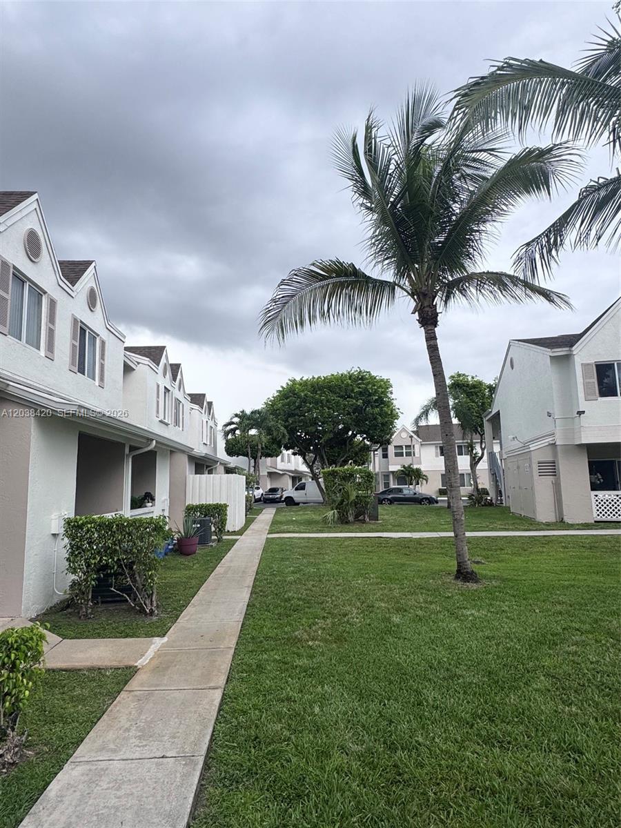 A sidewalk leads between two-story residential buildings with white stucco walls and green lawns — 17425 NW 67th Pl # 13, Hialeah FL 33015, HIALEAH, FL