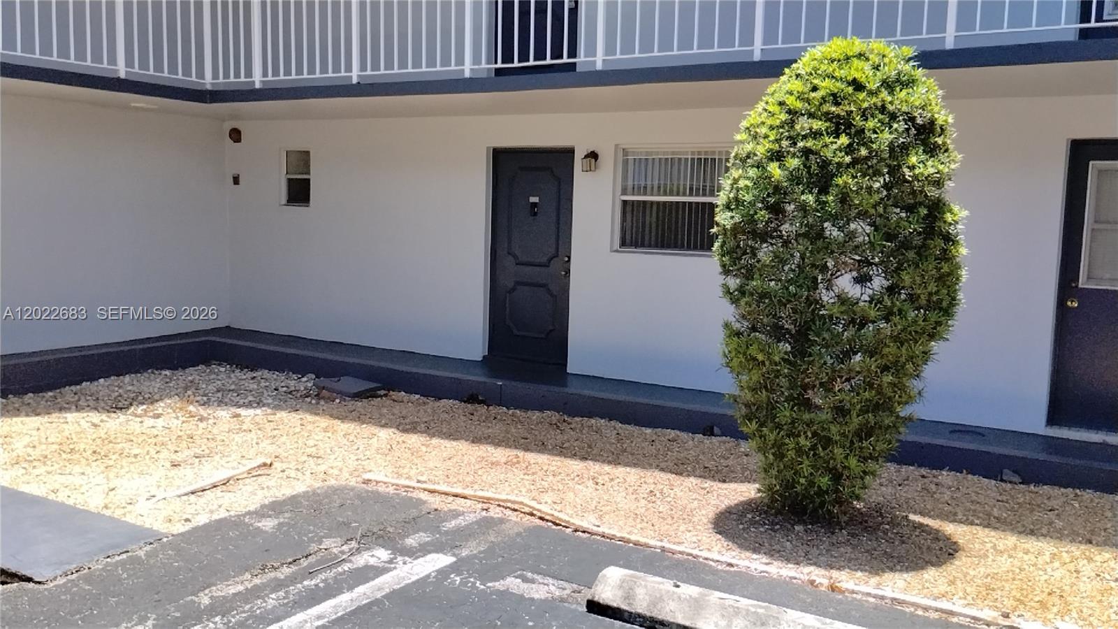 A ground-level apartment entrance features a dark door, a window, and a manicured shrub — 447 NE 195th St # 117, Miami FL 33179, MIAMI, FL