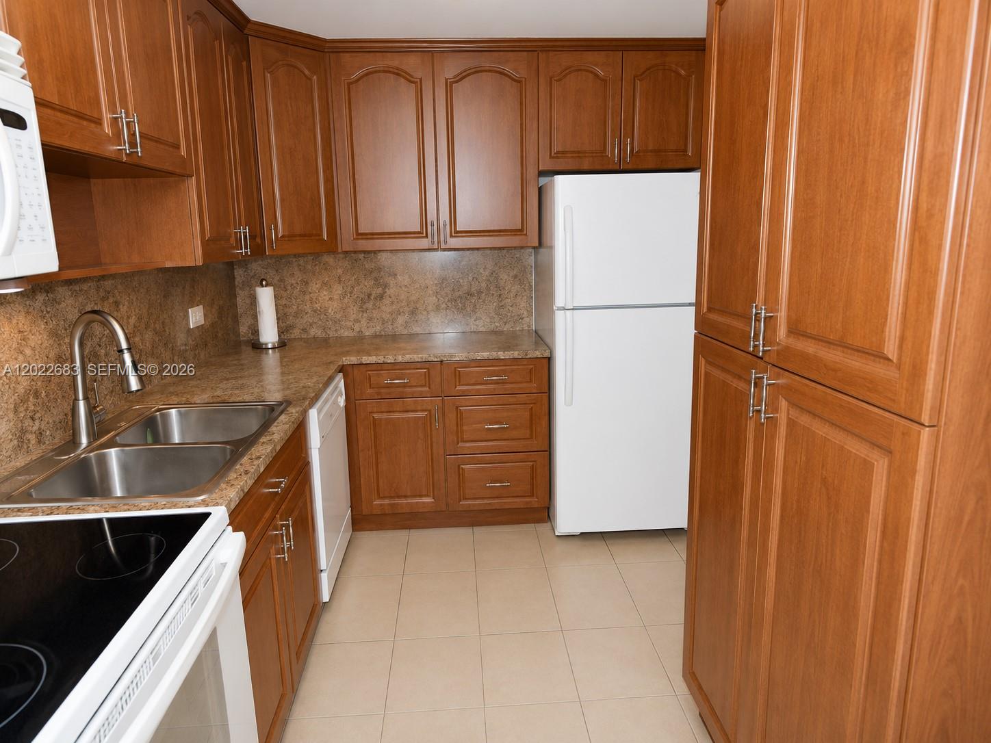 A kitchen features wood cabinets, laminate countertops, a white refrigerator, and a double sink — 447 NE 195th St # 117, Miami FL 33179, MIAMI, FL