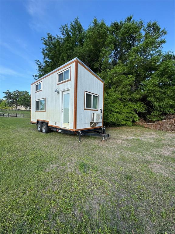A white tiny house on a trailer sits in a grassy field near trees — NW 4TH STREET, OCALA, FL
