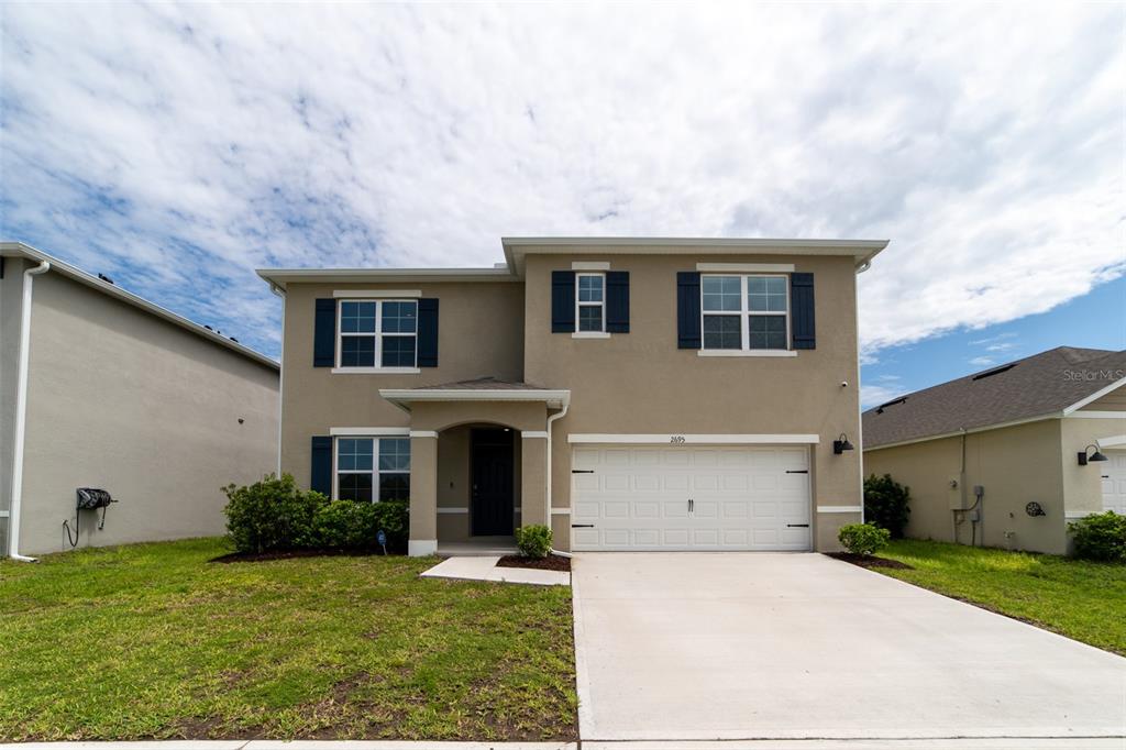 A two-story suburban house with a tan stucco exterior, dark shutters, and a two-car garage — 2695 HOUSE FINCH ROAD, HARMONY, FL