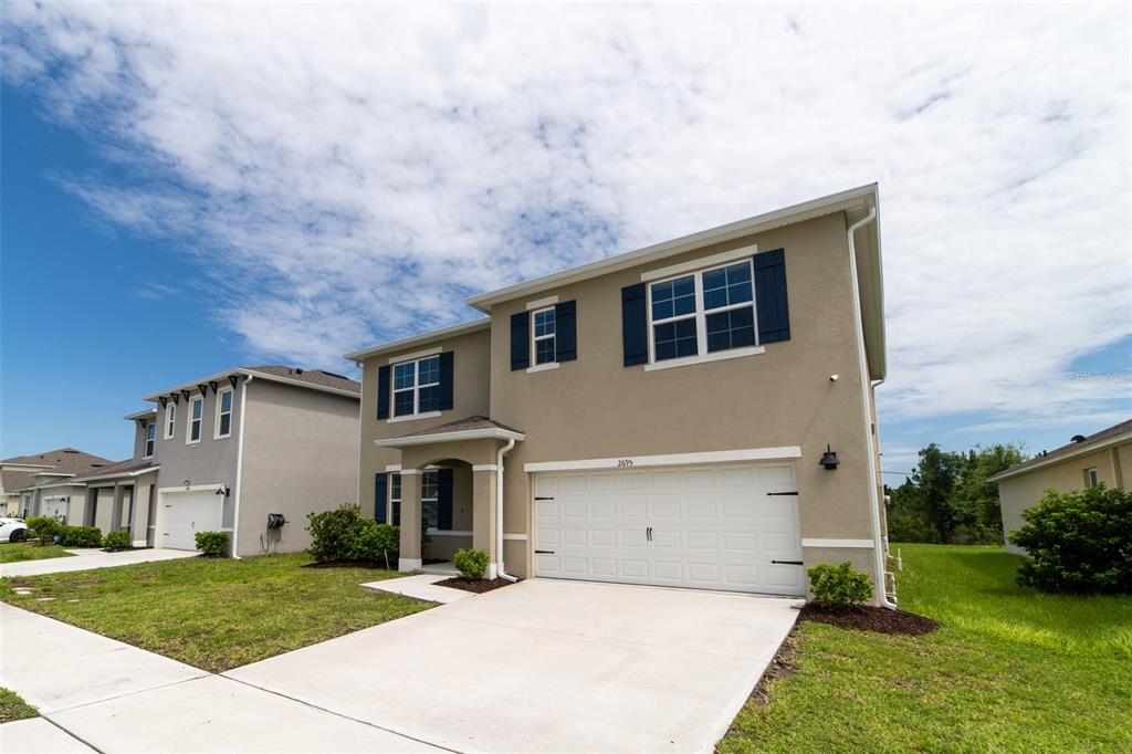 A two-story suburban house with a beige stucco exterior, dark shutters, and a two-car garage — 2695 HOUSE FINCH ROAD, HARMONY, FL