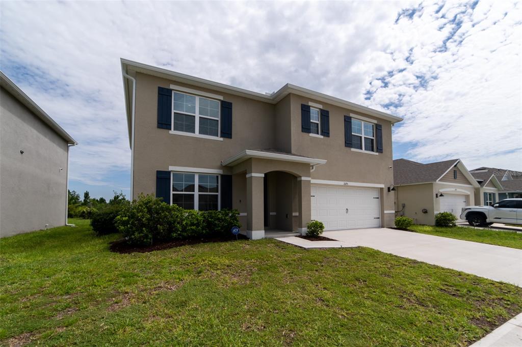 A two-story, tan suburban house with dark shutters, a two-car garage, and a front lawn — 2695 HOUSE FINCH ROAD, HARMONY, FL