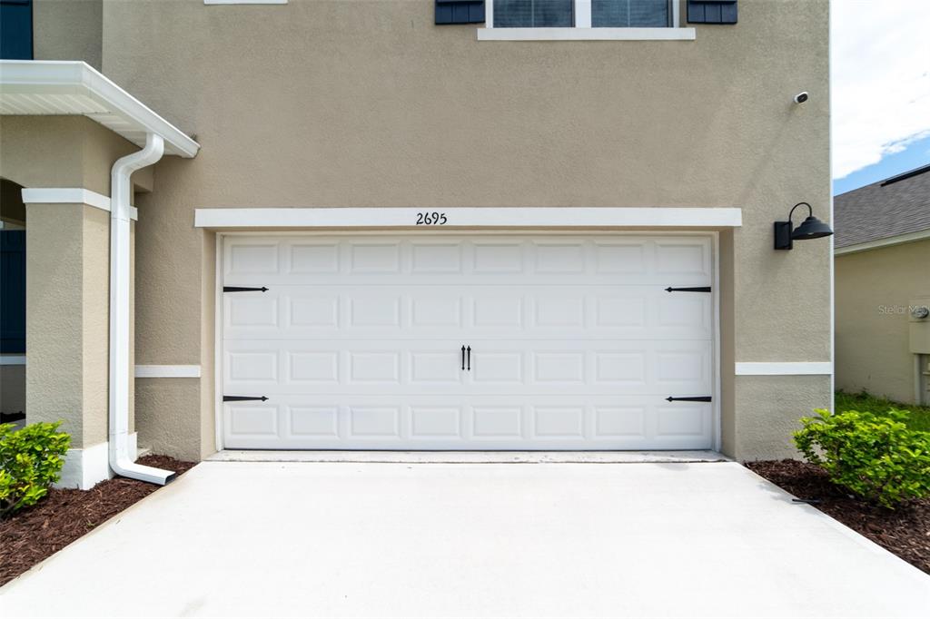 A beige house exterior features a white garage door with decorative black hardware — 2695 HOUSE FINCH ROAD, HARMONY, FL