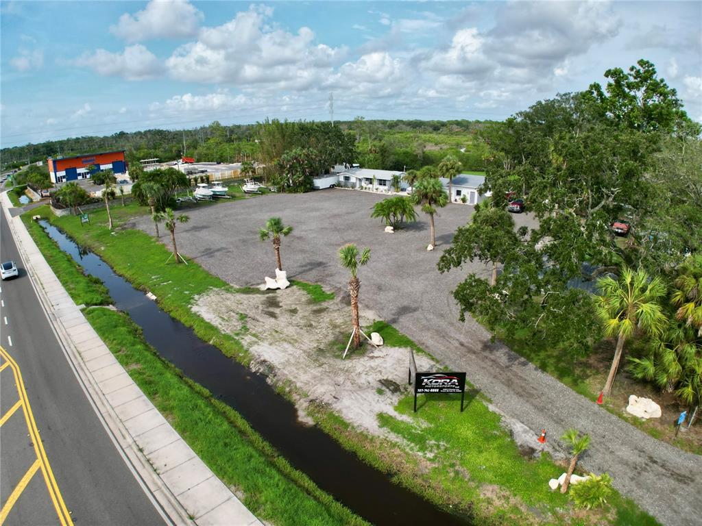 An aerial view shows a gravel lot with palm trees, a small building, and vehicles — 1322 N PINELLAS AVENUE, TARPON SPRINGS, FL