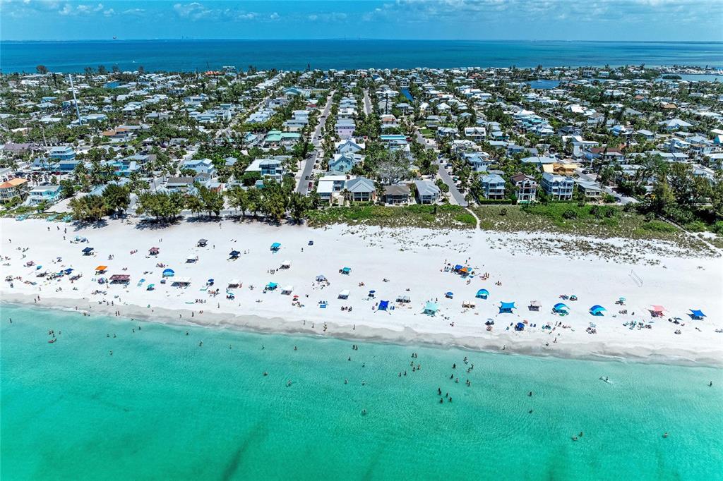 An aerial view shows a white sand beach with umbrellas and a coastal residential neighborhood — 101 PALM AVENUE UNIT 4, ANNA MARIA, FL