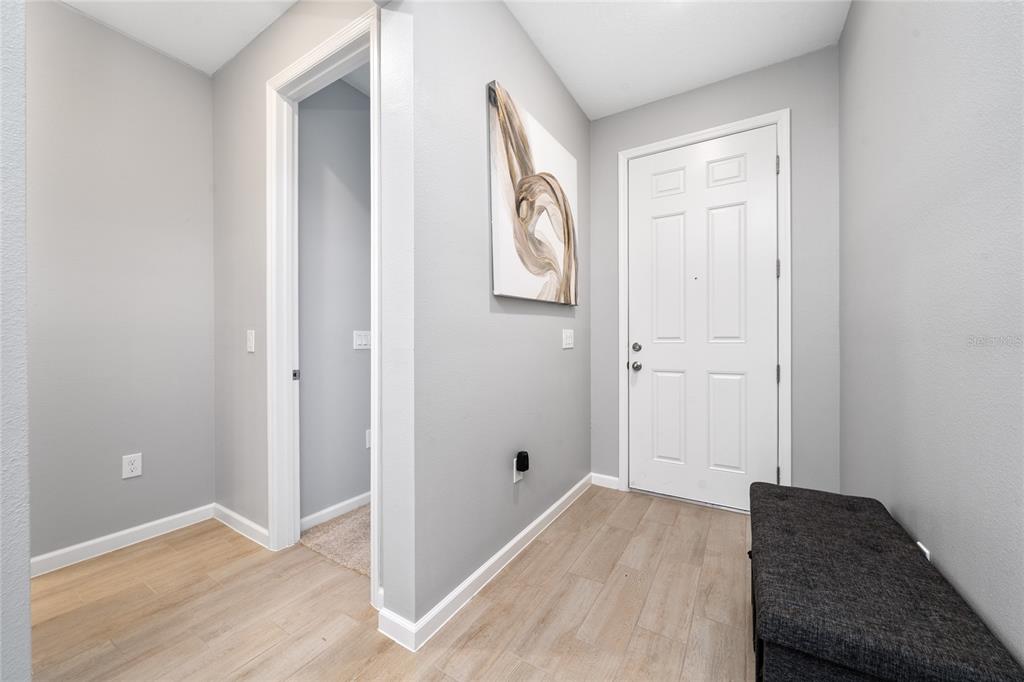An entryway features light wood-look tile flooring, a white door, and a dark storage bench — 1491 AUGUST GRAY DRIVE, KISSIMMEE, FL