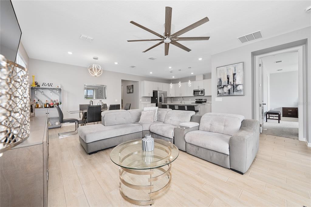 A modern open-concept living room features a gray sectional sofa, glass coffee table, and kitchen — 1491 AUGUST GRAY DRIVE, KISSIMMEE, FL