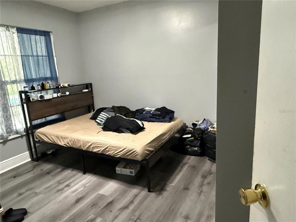 A bedroom features a metal bed frame, wood-look flooring, and a window with blue curtains — 2665 STALEY COURT, ORLANDO, FL