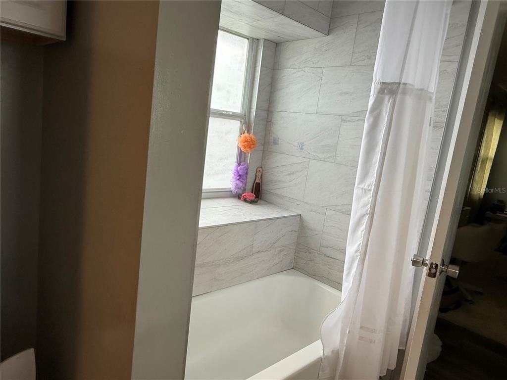A bathroom features a white bathtub, a window, and light-colored tiled walls — 2665 STALEY COURT, ORLANDO, FL