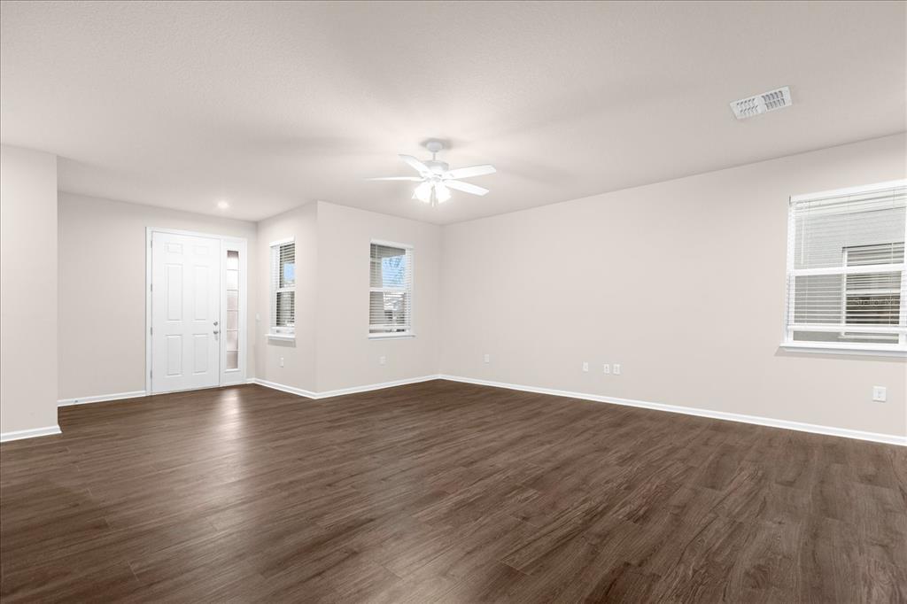 An empty living room features white walls, dark wood-look flooring, and a ceiling fan — 6162 GLORY BOWER DRIVE, WINTER GARDEN, FL