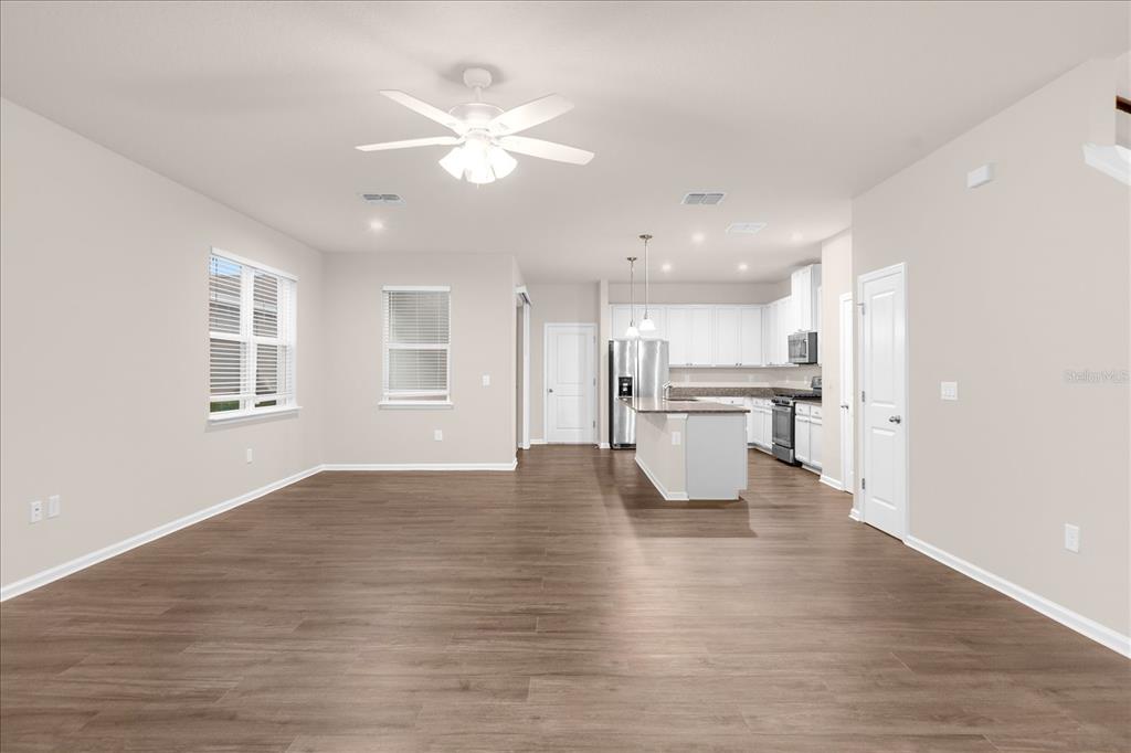 An open-concept living area with wood-look flooring leads to a kitchen with white cabinets — 6162 GLORY BOWER DRIVE, WINTER GARDEN, FL