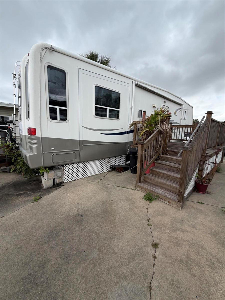 A white and gray recreational vehicle sits on a concrete pad next to wooden stairs — 5240 SE 67th Avenue SE, Okeechobee FL 34974, OKEECHOBEE, FL