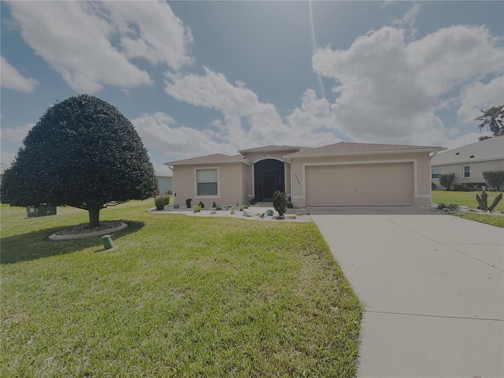 A single-story house with a beige stucco exterior, a two-car garage, and a large tree — 15596 SW 13TH CIRCLE, OCALA, FL