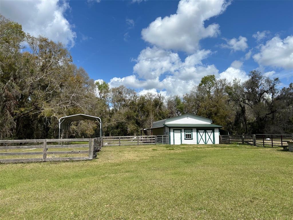 A grassy yard features a metal carport and a small white building with green trim — 13925 NW US-441, ALACHUA, FL
