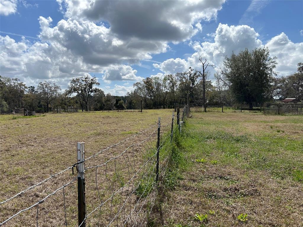 A wire fence runs through a grassy, open field under a cloudy blue sky — 13925 NW US-441, ALACHUA, FL