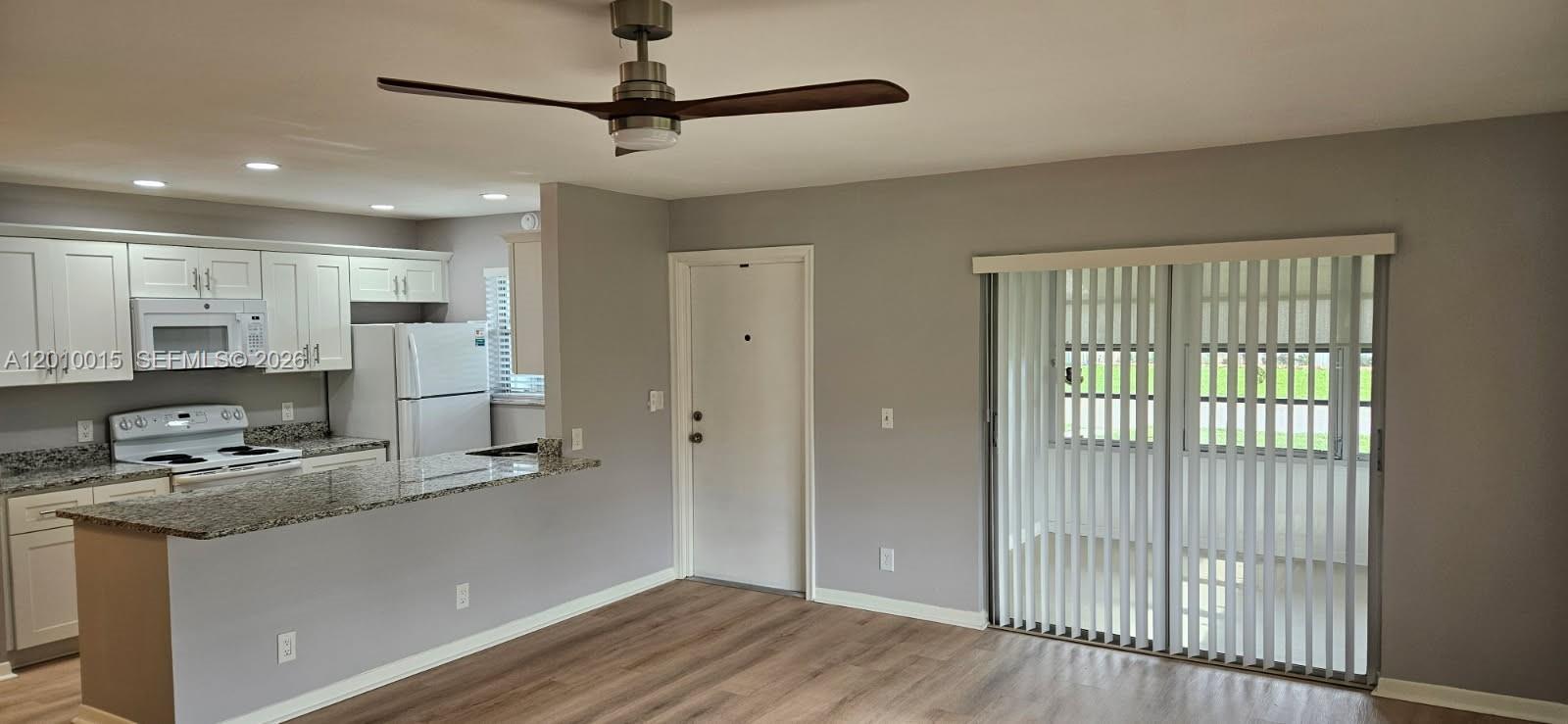 An open-concept kitchen with granite countertops overlooks a living area with sliding glass doors — 775 North Dr # A, Delray Beach FL 33445, DELRAY BEACH, FL