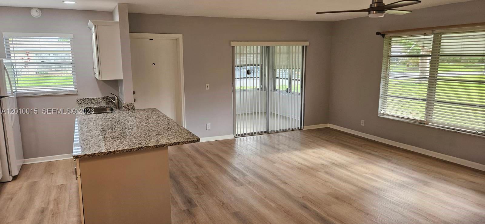 This open-concept living area features wood-look flooring, a granite kitchen counter, and sliding glass doors — 775 North Dr # A, Delray Beach FL 33445, DELRAY BEACH, FL