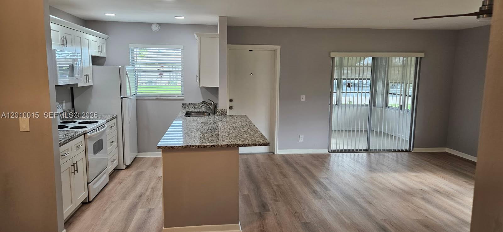 A kitchen with white cabinets and granite countertops opens into a living area with flooring — 775 North Dr # A, Delray Beach FL 33445, DELRAY BEACH, FL