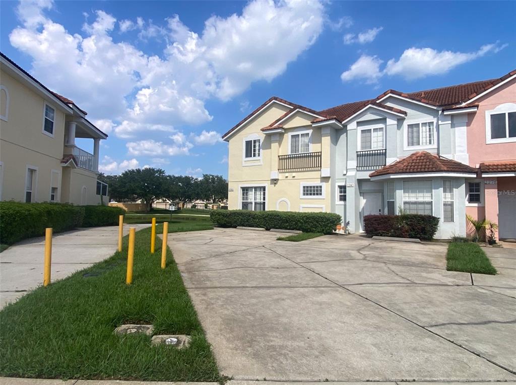 A multi-story townhouse complex features a concrete driveway, yellow and light-colored siding, and tiled roofs — 1282 S BEACH CIRCLE, KISSIMMEE, FL