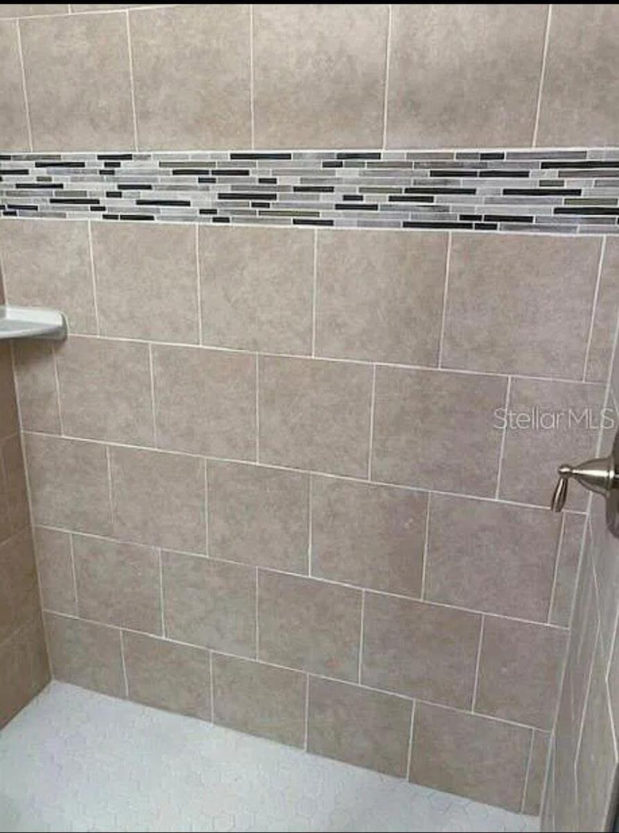 A shower with beige square wall tiles and a horizontal decorative glass mosaic accent strip — 640 E Grapefruit Avenue, FL 33850, FL