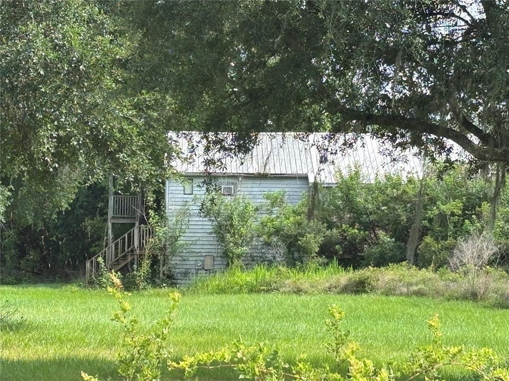 A weathered, light-colored wooden building with an exterior staircase stands in a grassy field — 4670 ANDERSON ROAD, KISSIMMEE, FL