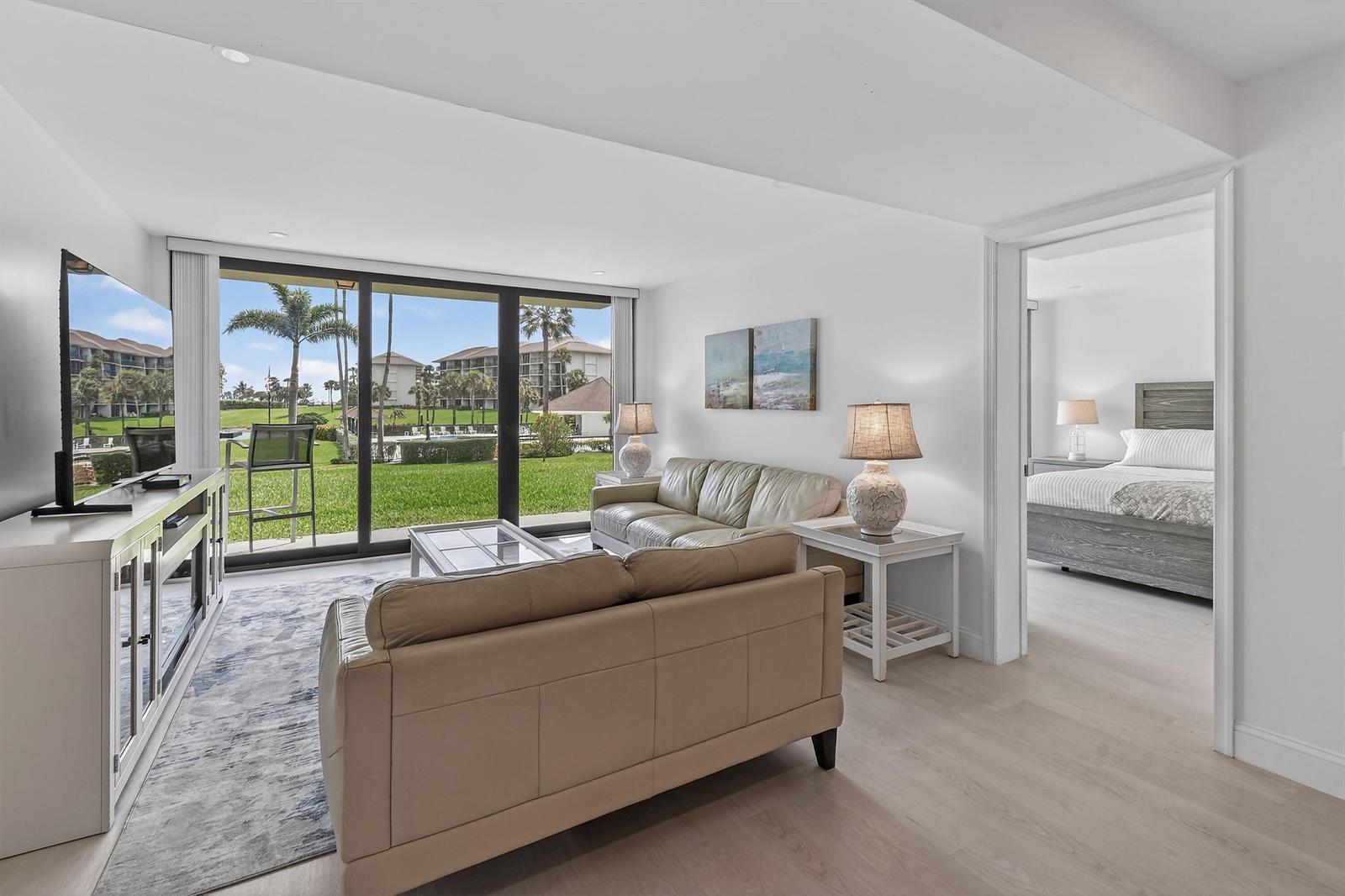 A living room with light-colored sofas and a view of a pool and palm trees — 301 S Seas Drive # 104, Jupiter FL 33477, JUPITER, FL